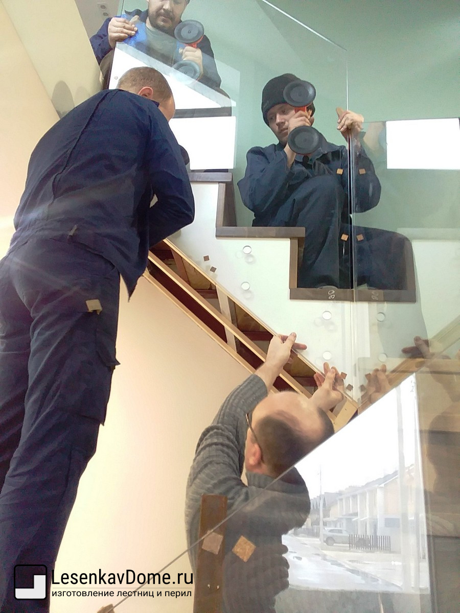 Монтажники закрепляют стеклянную секцию перил к лестничному маршу